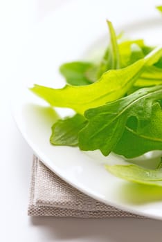 Fresh arugula leaves in white plate on table cloth. Selective focus. Shallow DOF