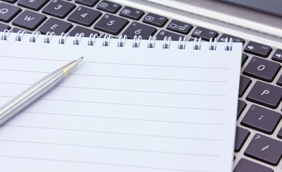 a notebook and pen lie on the keyboard of computer