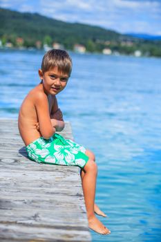 Summer vacation  at the lake - happy little boy resting on the pier and watching on the yacht
