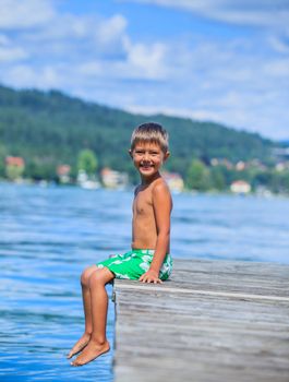 Summer vacation  at the lake - happy little boy resting on the pier and watching on the yacht
