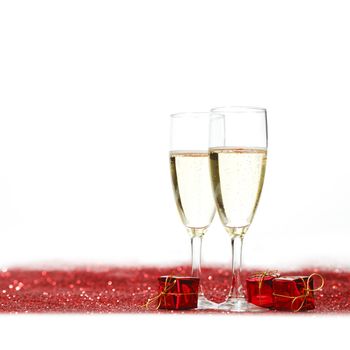 Glasses with Champagne and gifts on red glitters isolated on white background