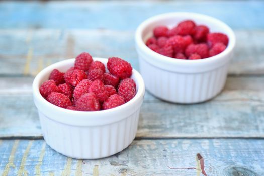 much fresh ripe raspberry in a white bowl on a wooden background