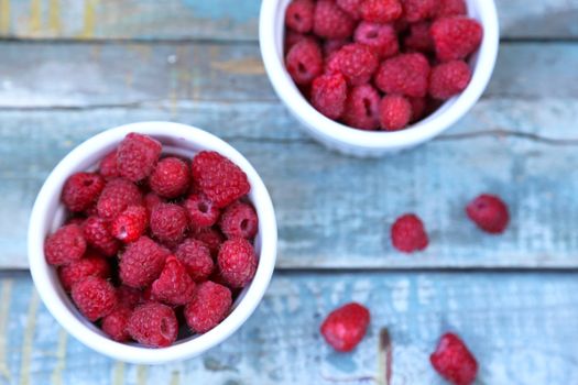 much fresh ripe raspberry in a white bowl on a wooden background