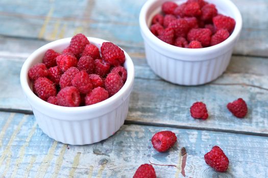 much fresh ripe raspberry in a white bowl on a wooden background