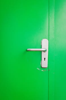 Metal door handle on green steel door, with keyhole