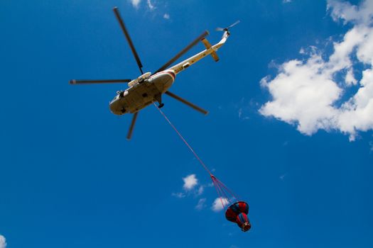 Firefighting helicopter with fire bucket flies against a clear blue sky