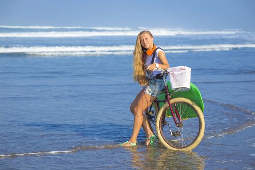 Young girl with surfboard and bicycle on the beach.