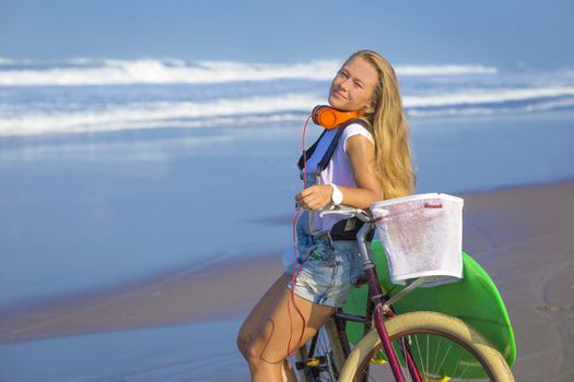 Young girl with surfboard and bicycle on the beach.