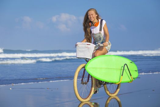 Young girl with surfboard and bicycle on the beach.