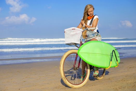 Young girl with surfboard and bicycle on the beach.