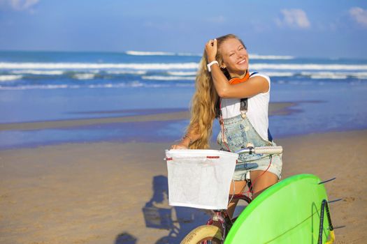 Young girl with surfboard and bicycle on the beach.