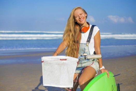 Young girl with surfboard and bicycle on the beach.