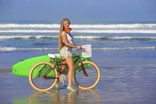 Young girl with surfboard and bicycle on the beach.