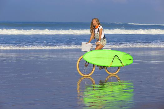 Young girl with surfboard and bicycle on the beach.