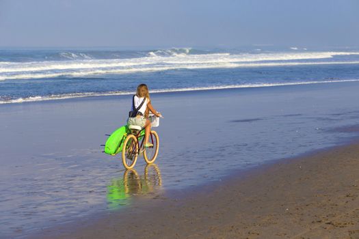 Young girl with surfboard and bicycle on the beach.