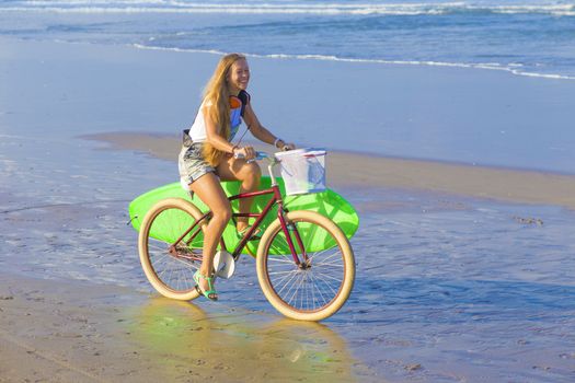 Young girl with surfboard and bicycle on the beach.