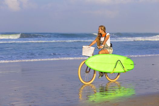 Young girl with surfboard and bicycle on the beach.