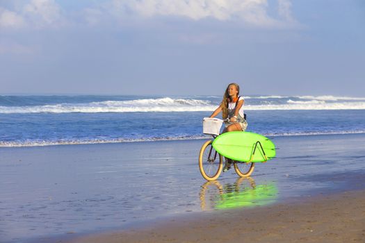 Young girl with surfboard and bicycle on the beach.