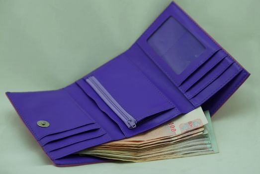 Purple wallet has many bills inside, placed on white background.                             