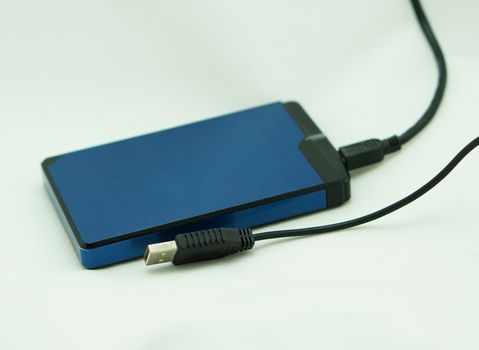 Blue battery backup is used to recharge a mobile phone, placed on white table.                               