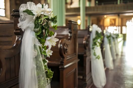 Wedding decoration white flowers and green leafs hanging on the church benches