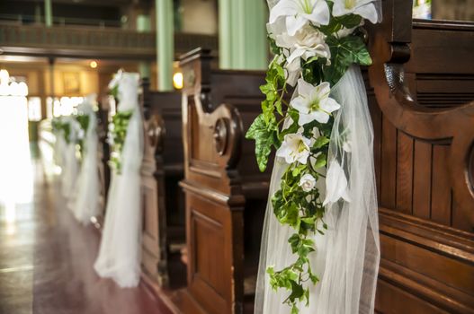 Wedding decoration white flowers and green leafs hanging on the church benches