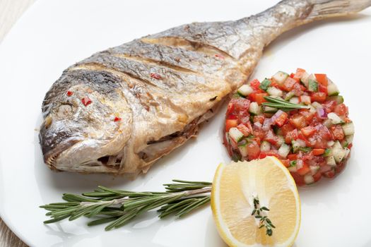 Gourmet Mediterranean seafood dish. Grilled fish gilthead served with vegetable salsa, lemon, rosemary on white plate top view