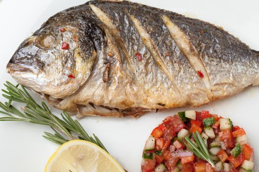 Gourmet Mediterranean seafood dish. Grilled fish gilthead served with vegetable salsa, lemon, rosemary on white plate top view