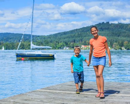 Summer vacation  at the lake - two happy kids walking on the pier and watching on the yacht