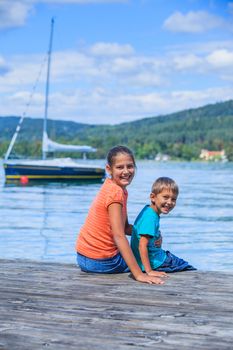 Summer vacation  at the lake - two happy kids resting on the pier and watching on the yacht