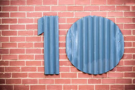 The number ten cut out of corrugated iron and placed on a face brick wall.