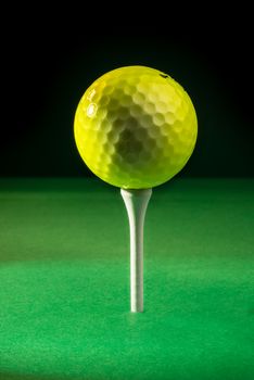 A yellow golf ball positioned on top of a tee, ready for the tee shot.