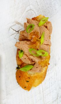 Tapas Bruschetta with Delicious Liver Pate and Crushed Spring Onion on Garlic Bread closeup on White Wooden background. Top View