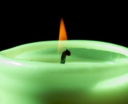 Big Green Candle Burning with Yellow Flame closeup on Black Background. Focus on Flame