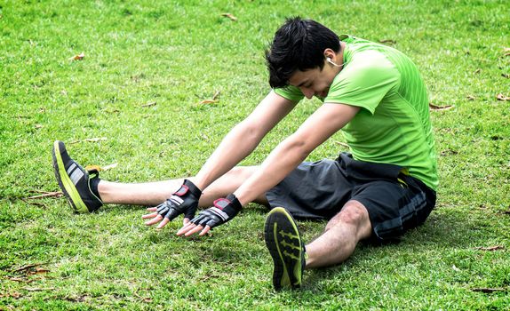 Young man at the park warming and stretching on the grass