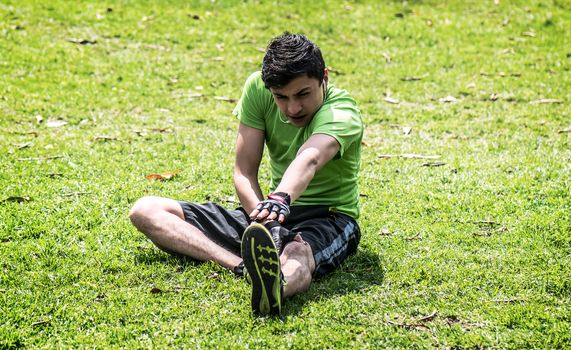 Young man at the park warming and stretching on the grass 