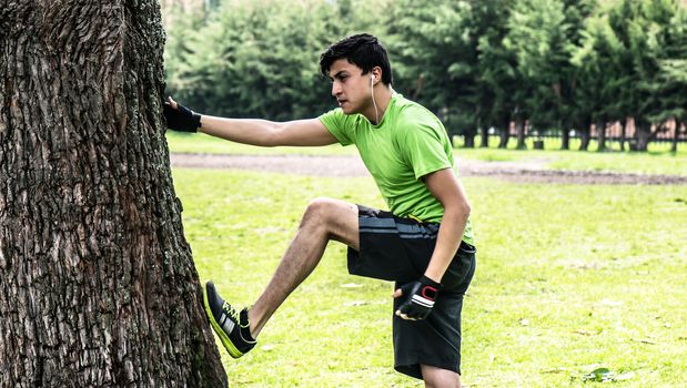 Young man at the park warming and stretching with a tree