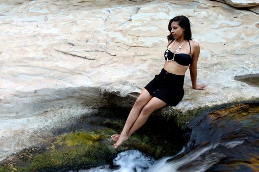 Hispanic woman with bikini sitting next to a waterfall.