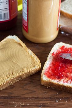 A peanut butter and jelly sandwich being constructed on a wooden table.