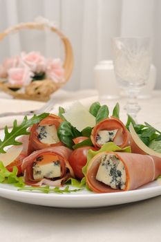 Appetizer rolls with jamon, blue cheese in the mix of lettuce and parmesan slices under