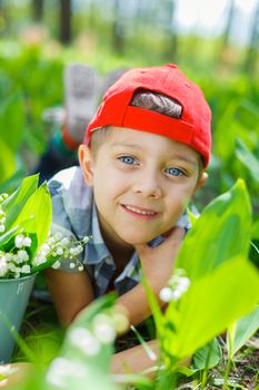 Cute little boy with lilies of the valley in forest on spring day