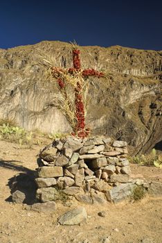 Christian cross wrapped around with flowers on peruvian arid landscape near Canon del Colca