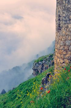 Tower stone wall above mist on green landscape of mountainous Karabakh