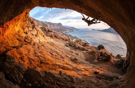 Male rock climber climbing along a roof in a cave at sunset