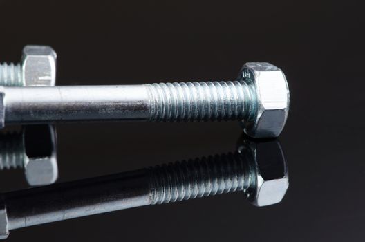 Two metal screws with nice reflection on black background.