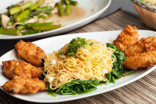 Thai style fried chicken wings on a round white plate with egg noodles and spinach.