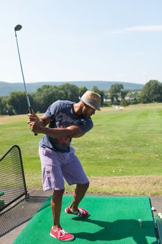 Athletic golfer swinging at the driving range dressed in casual attire.