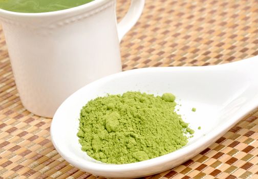 Matcha green tea on spoon by a cup of tea