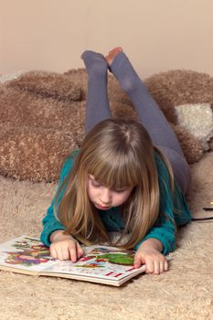 A cheerful girl is reading a book lying on the thick carpet