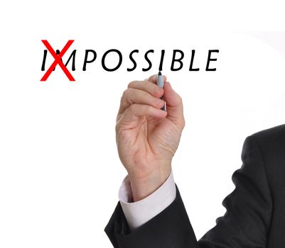 Businessman in suit drawing text of the word impossible with red mark through part of the word making it now possible